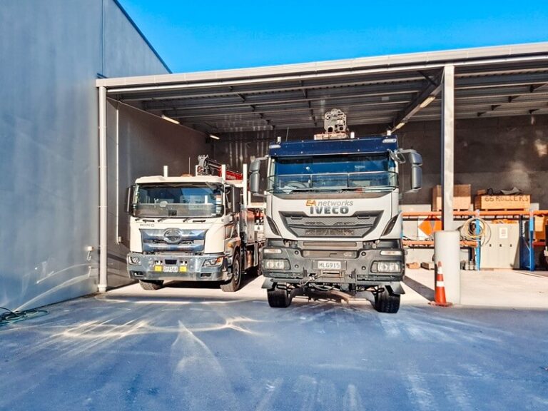 A salesman and a customer shaking hands standing in front of three lines crane trucks that are being handed over