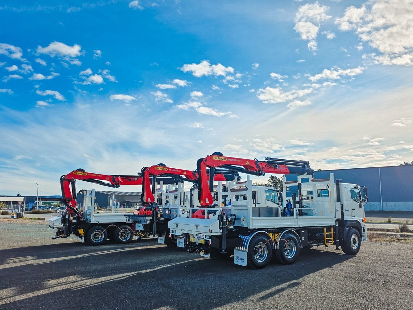 A salesman and a customer shaking hands standing in front of three lines crane trucks that are being handed over