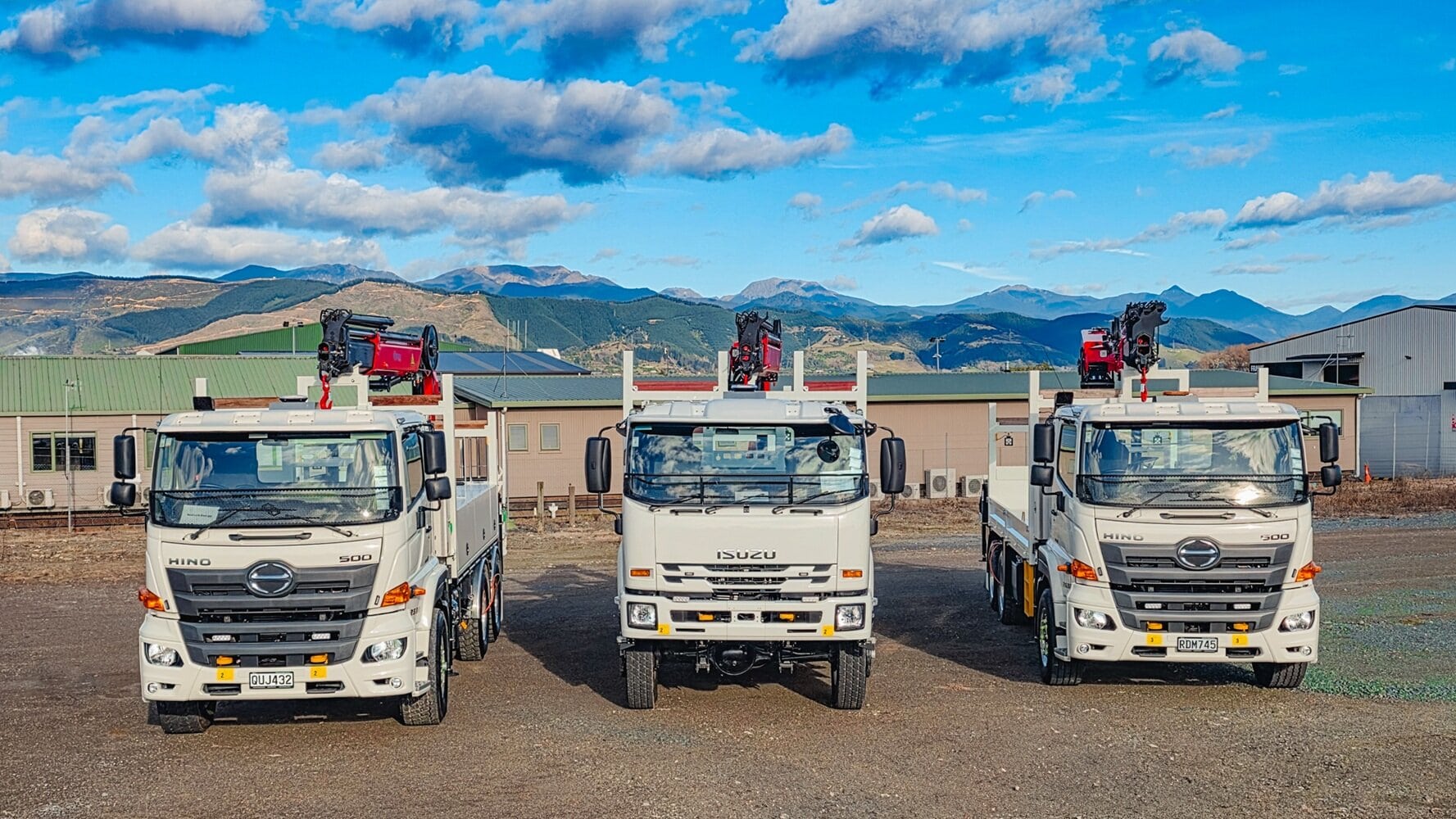 A salesman and a customer shaking hands standing in front of three lines crane trucks that are being handed over