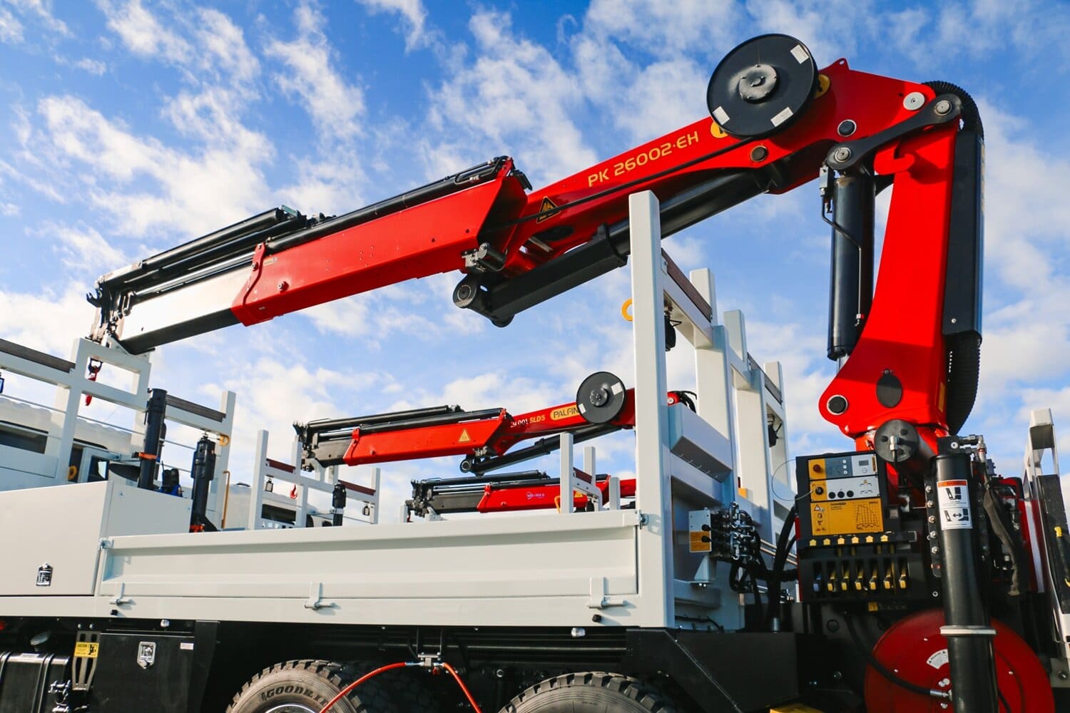 A salesman and a customer shaking hands standing in front of three lines crane trucks that are being handed over