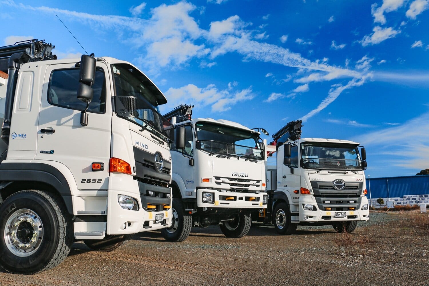 A salesman and a customer shaking hands standing in front of three lines crane trucks that are being handed over