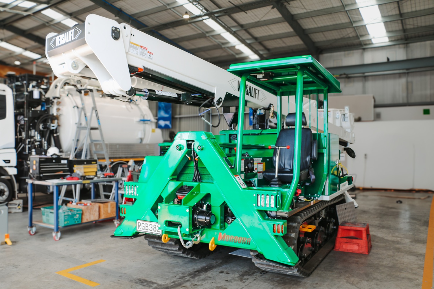 A specialist utility truck with tracks instead of wheels and a Versalift boom parked in a workshop with the boom stowed.