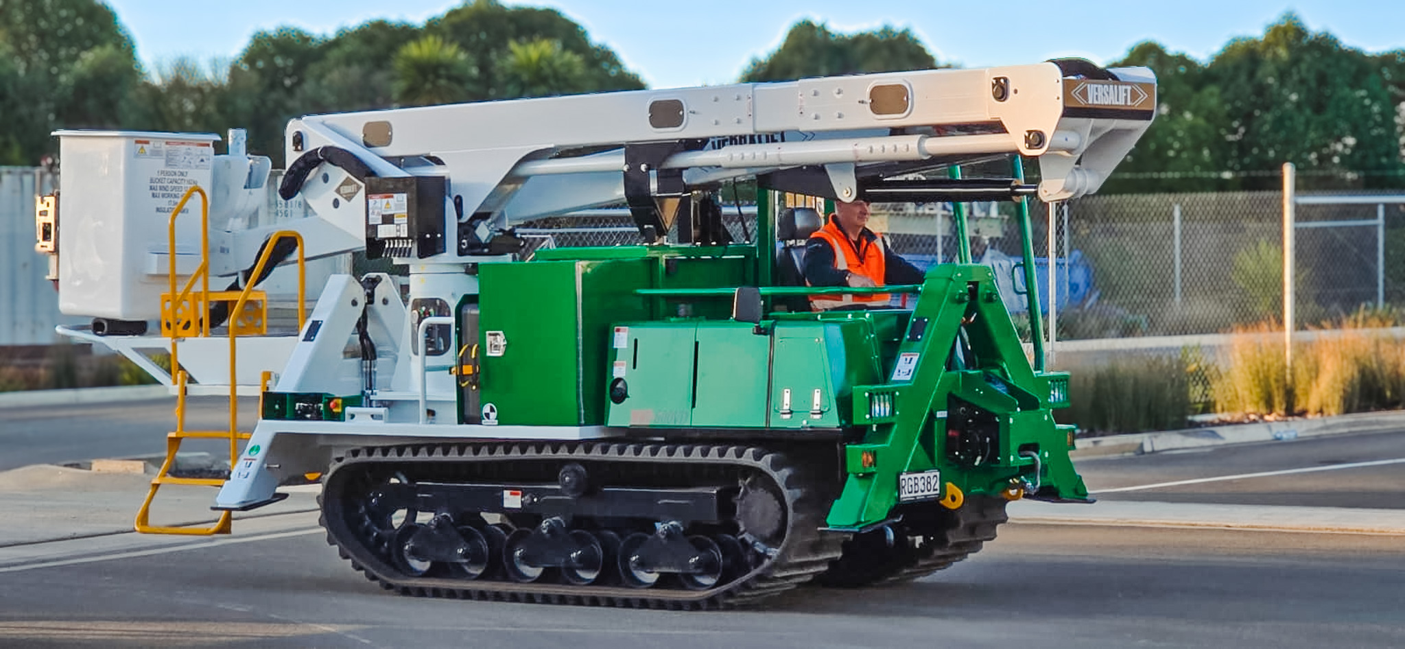 A specialist utility truck with tracks instead of wheels and a Versalift boom parked in a workshop with the boom stowed.