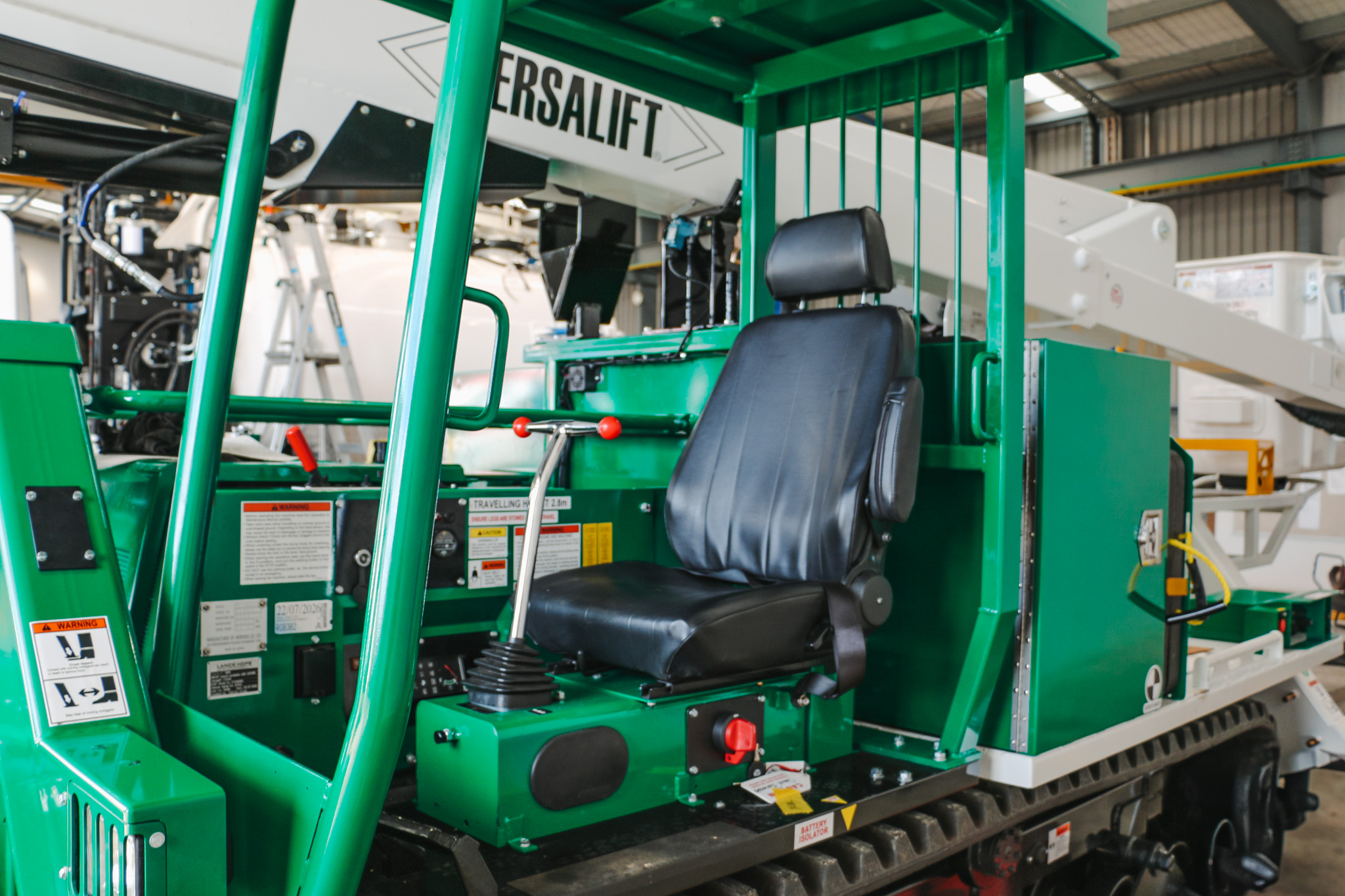 A specialist utility truck with tracks instead of wheels and a Versalift boom parked in a workshop with the boom stowed.