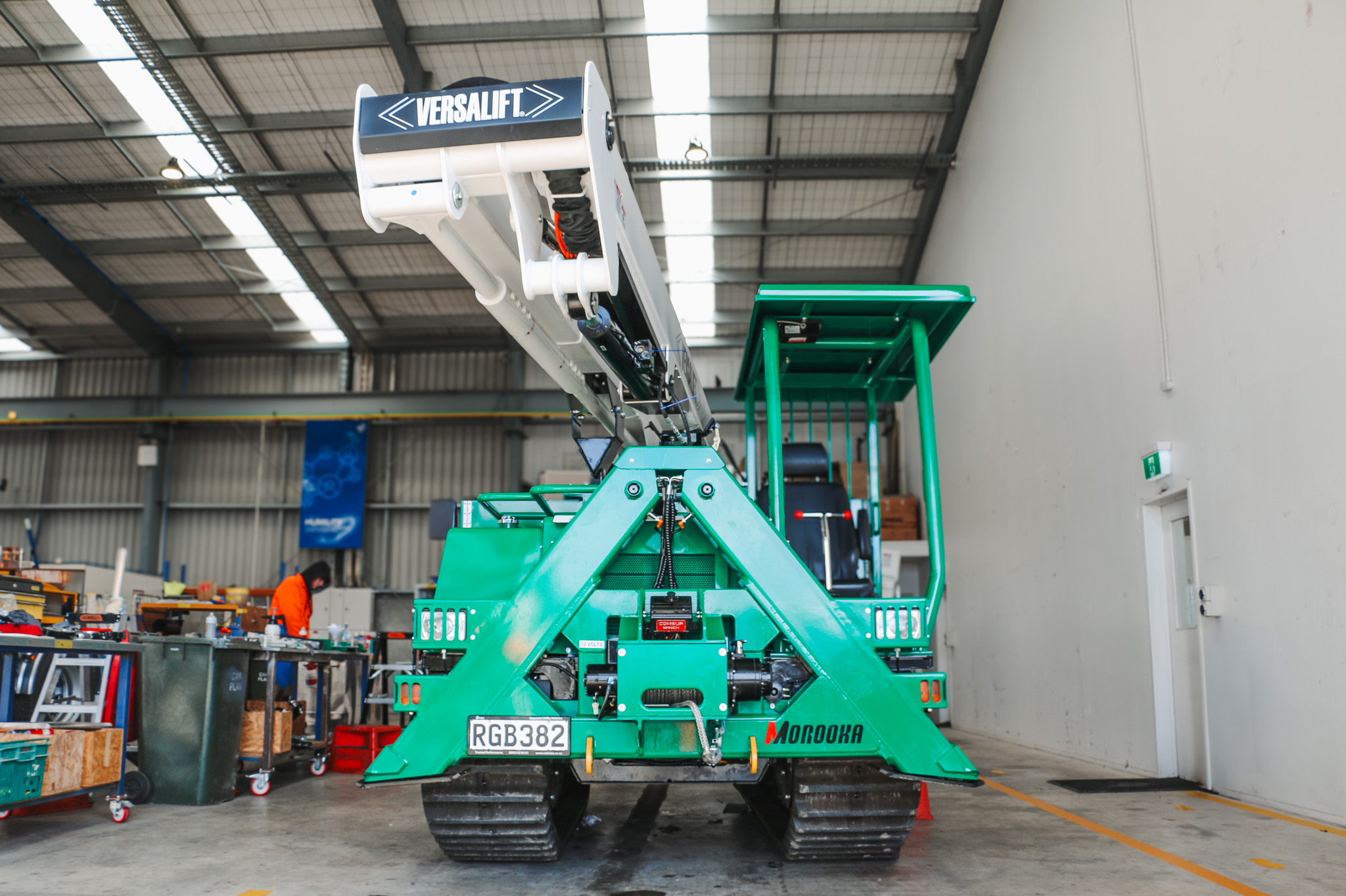 A specialist utility truck with tracks instead of wheels and a Versalift boom parked in a workshop with the boom stowed.
