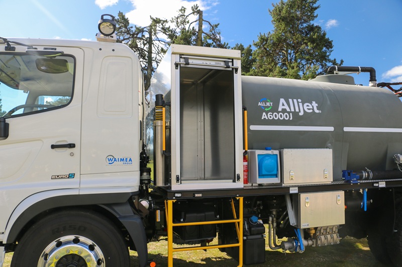 Here's our September #TruckoftheMonth - Waimea's newest and sharpest unit! A large utility truck parked on the grass in front of a body of water, equipped with jetting equipment, carrying a 6000L tank and two hose reels with a set of nozzles for jetting out drains and culverts.