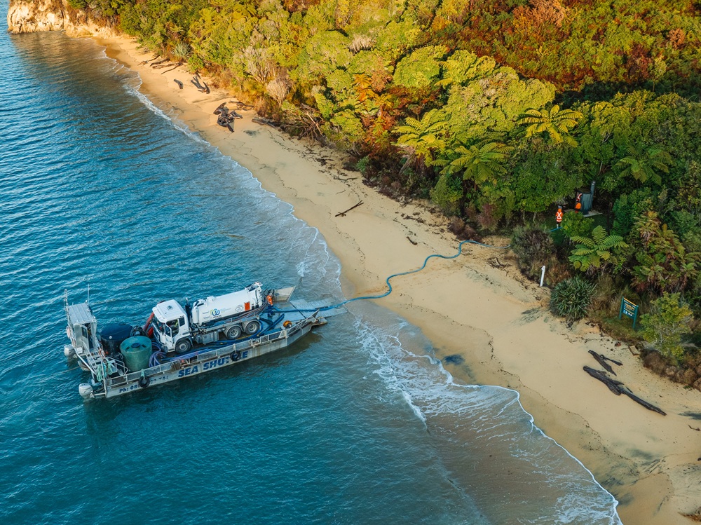 TOTM Aug2025_gallery (4) An Allvac® vacuum tanker truck on the back of a barge backed into a beautiful bay in the Abel Tasman National Park, removing liquid waste from a campsite.