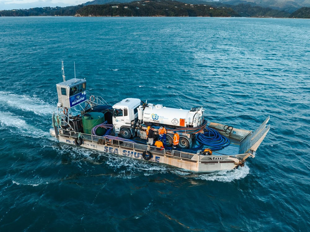 TOTM Aug2025_gallery (5) An Allvac® vacuum tanker truck on the back of a barge backed into a beautiful bay in the Abel Tasman National Park, removing liquid waste from a campsite.