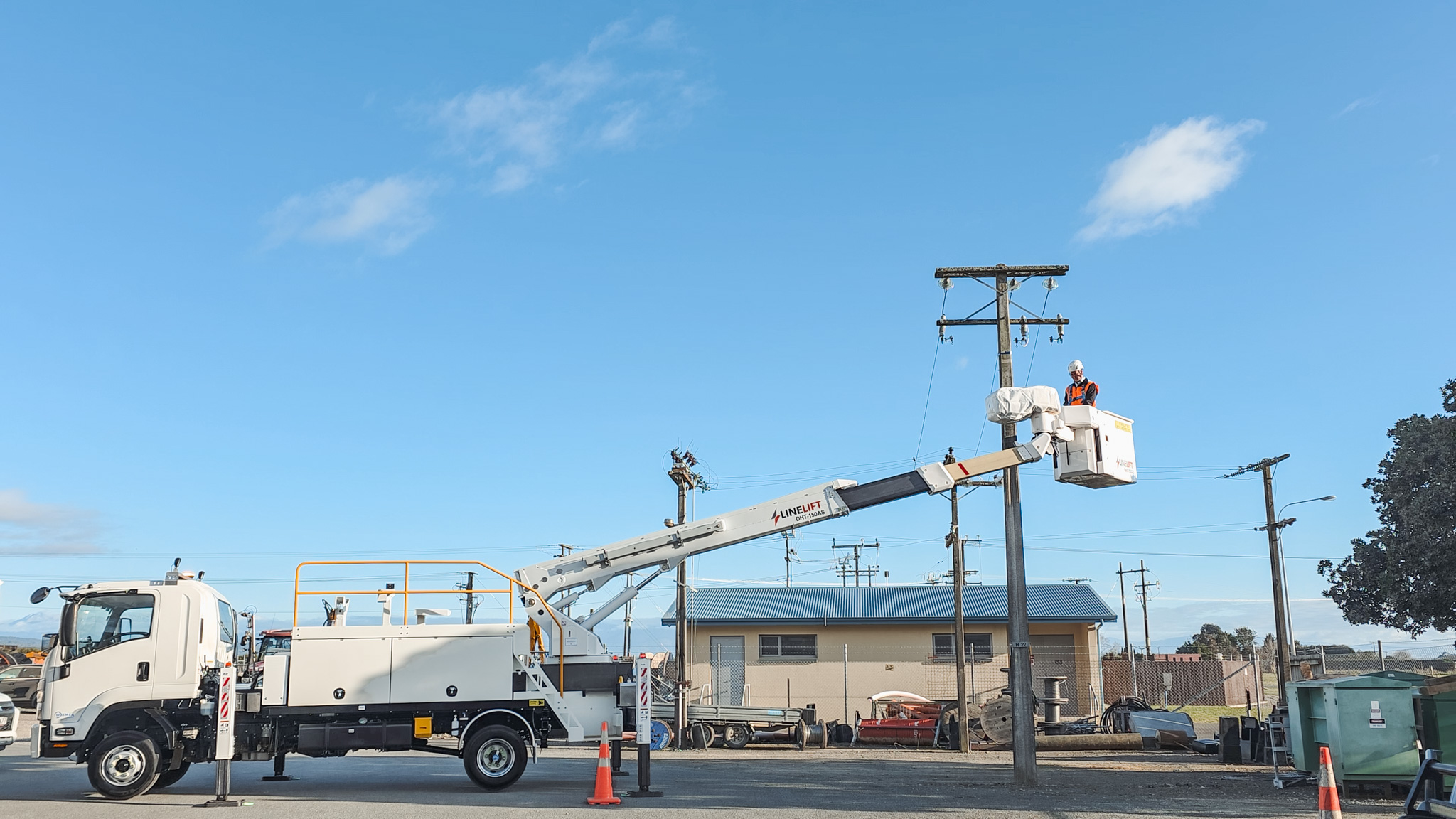 Full shot 2 An upward angle of a Linelift® elevated work platform with its boom extended bucket positioned near a power pole against a blue sky