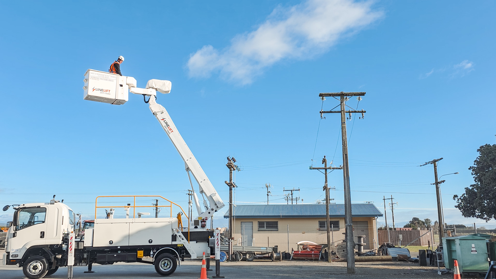 Full shot 3 An upward angle of a Linelift® elevated work platform with its boom extended bucket positioned near a power pole against a blue sky