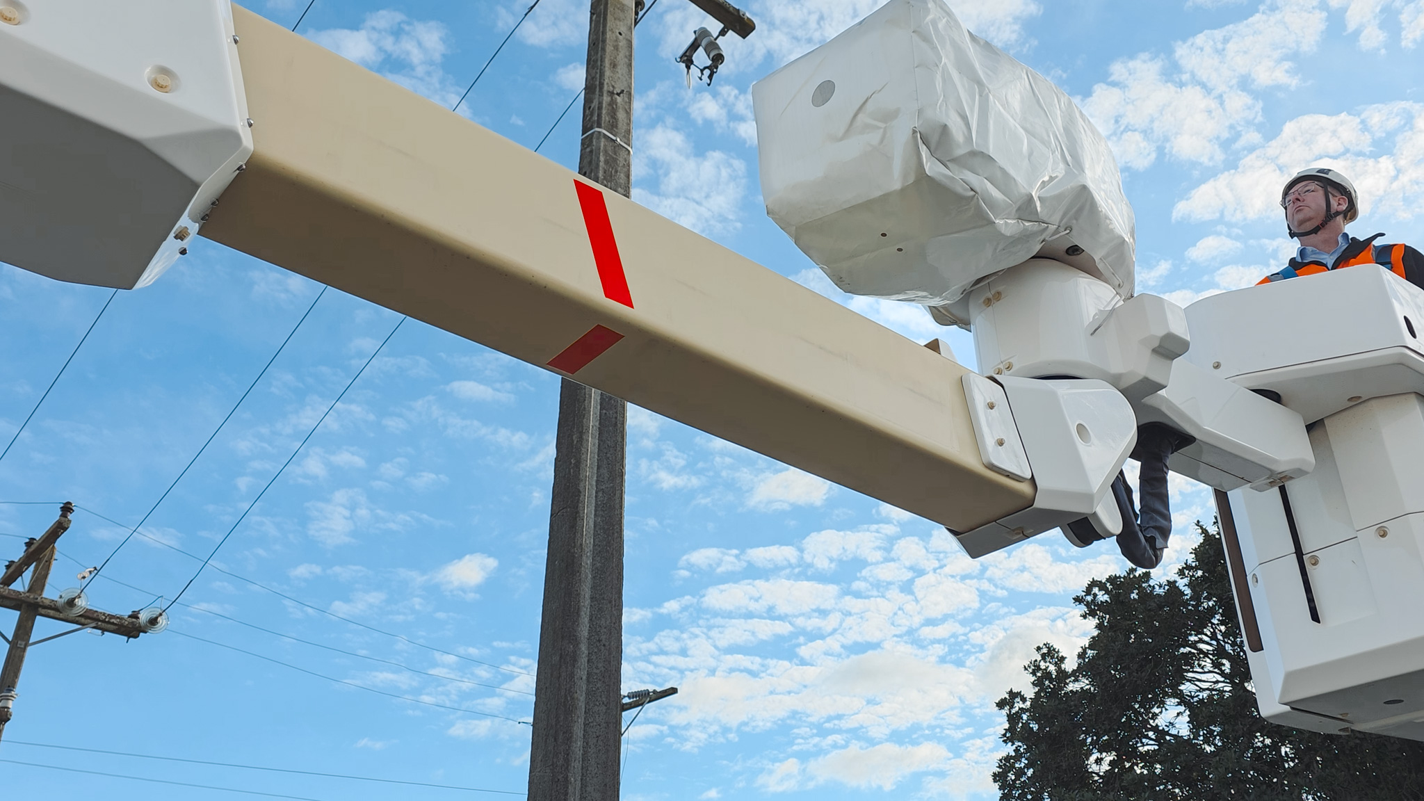An upward angle of a Linelift® elevated work platform with its boom extended bucket positioned near a power pole against a blue sky