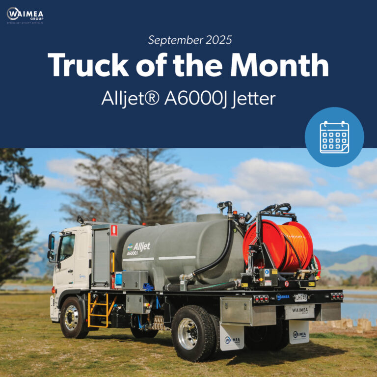 A large utility truck parked on the grass in front of a body of water, equipped with jetting equipment, carrying a 6000L tank and two hose reels with a set of nozzles for jetting out drains and culverts.