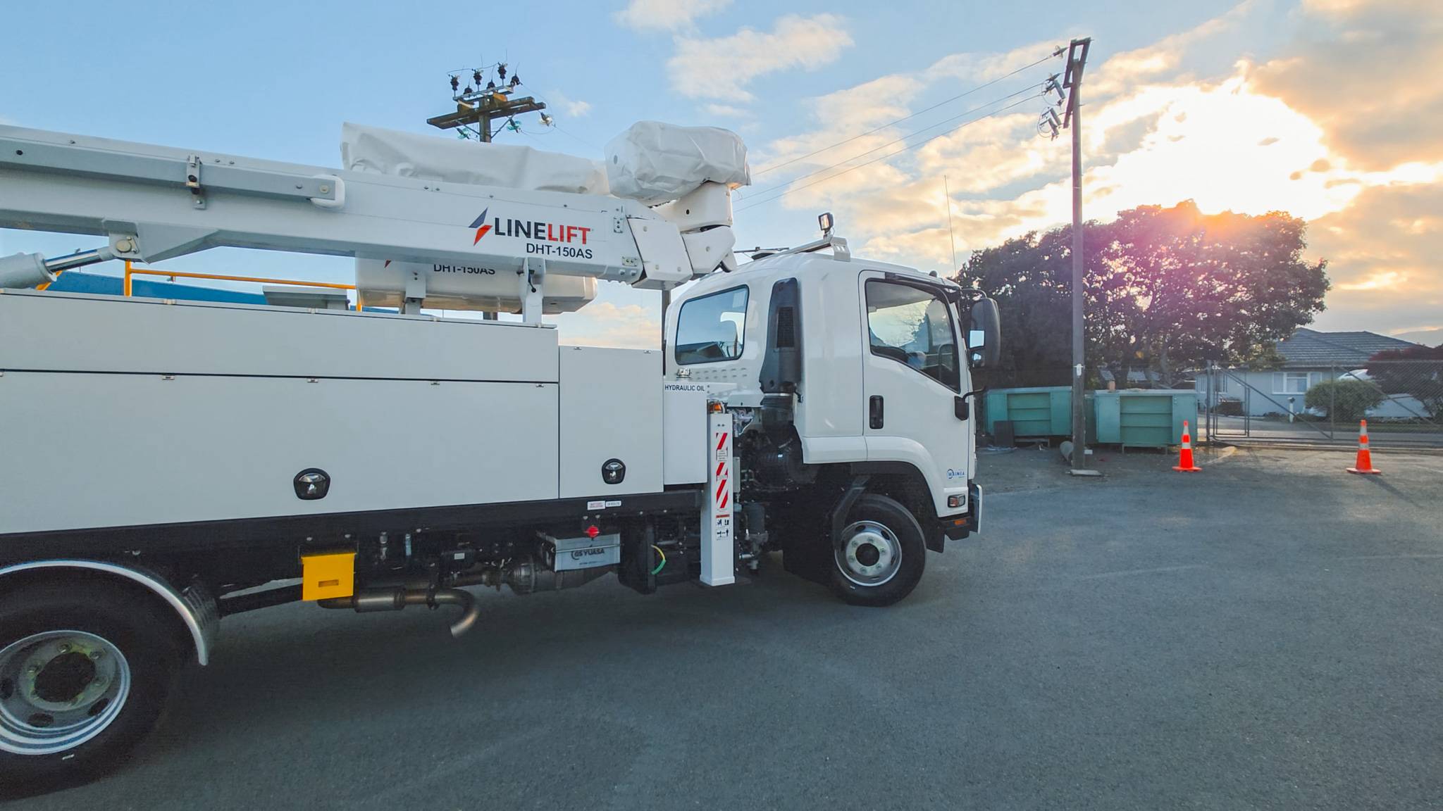 An upward angle of a Linelift® elevated work platform with its boom extended bucket positioned near a power pole against a blue sky