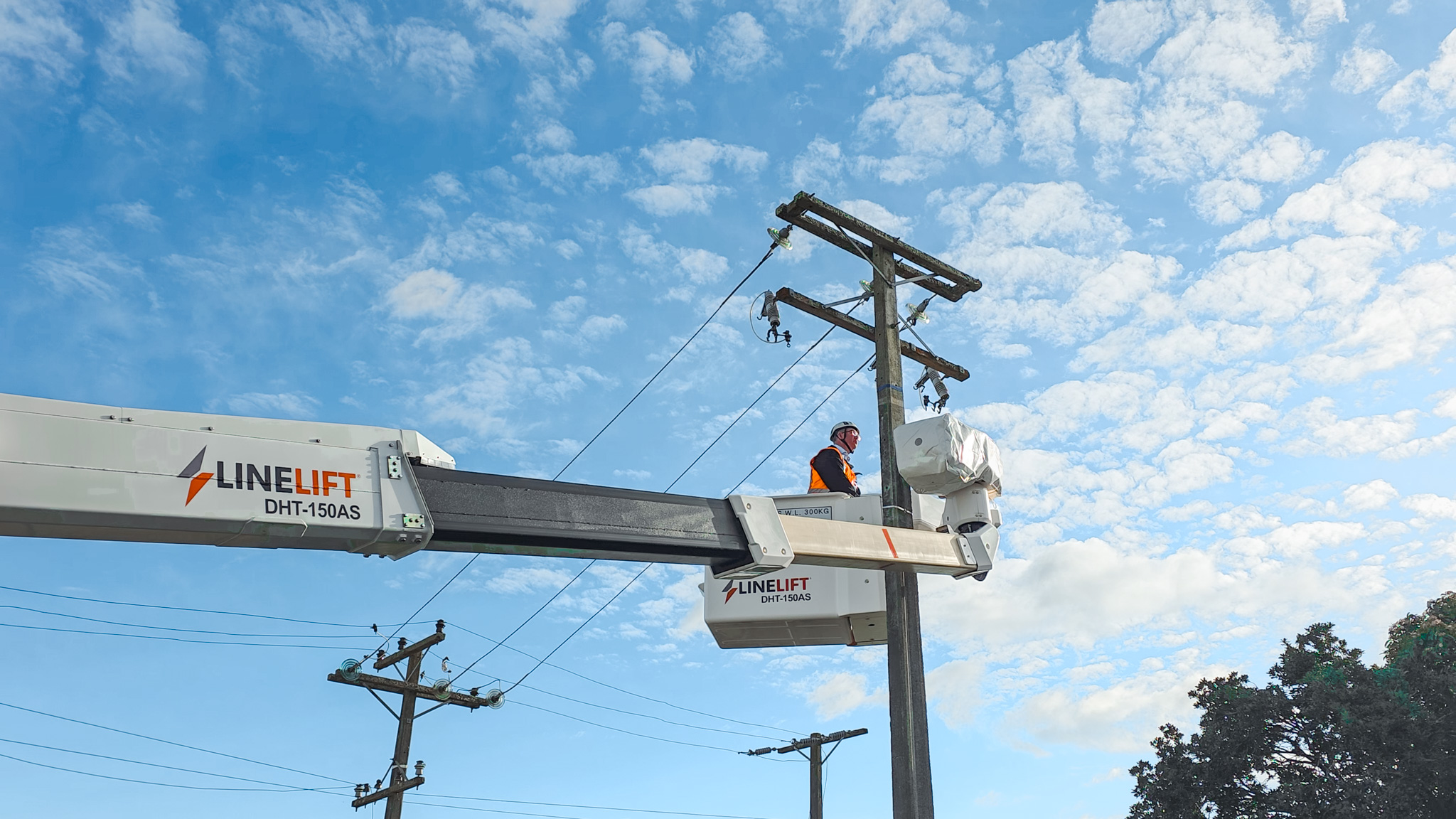 An upward angle of a Linelift® elevated work platform with its boom extended bucket positioned near a power pole against a blue sky