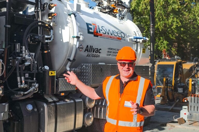 A man in hi-vis gear and a hard hat standing in front of an Allvac® AV7000H hydrovac truck and other drilling equipment on a construction site