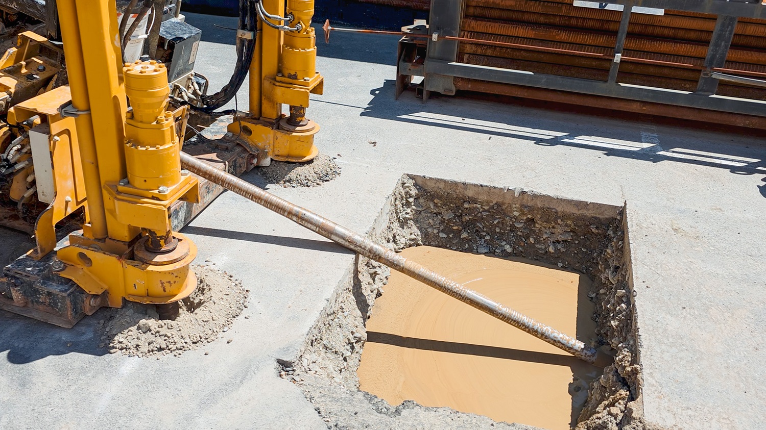 A man in hi-vis gear and a hard hat standing in front of an Allvac® AV7000H hydrovac truck and other drilling equipment on a construction site