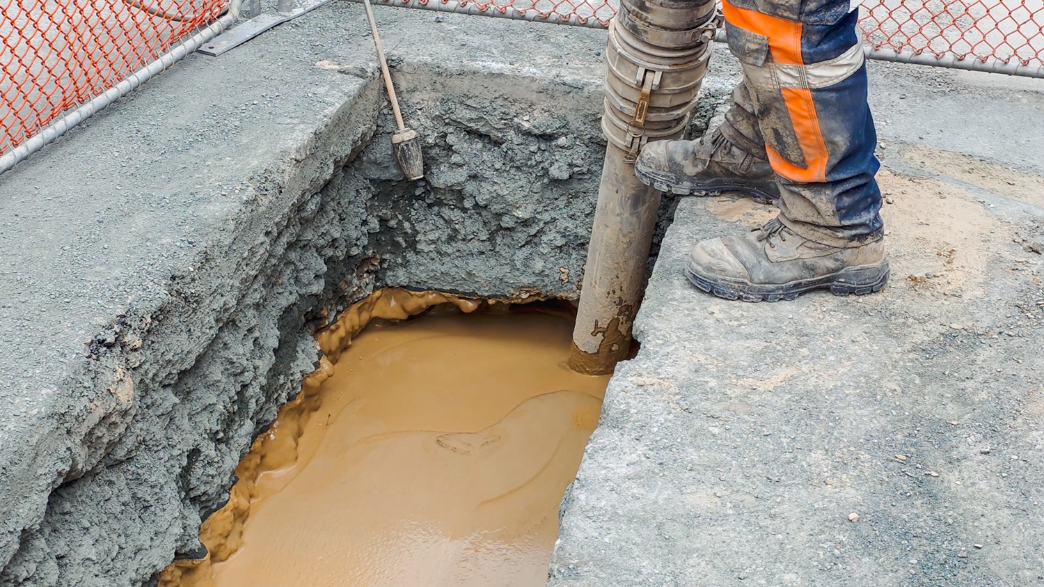 A man in hi-vis gear and a hard hat standing in front of an Allvac® AV7000H hydrovac truck and other drilling equipment on a construction site
