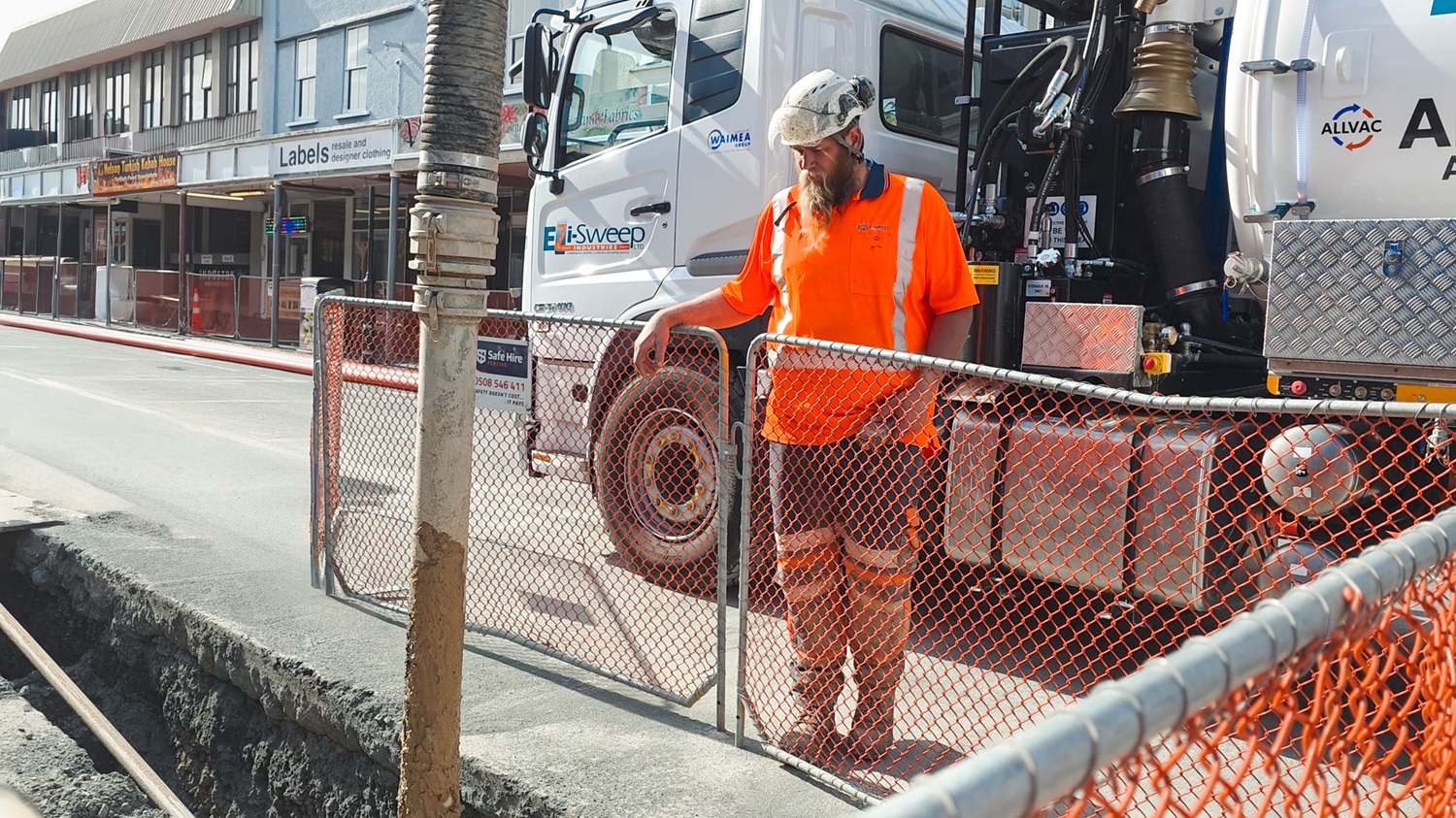 A man in hi-vis gear and a hard hat standing in front of an Allvac® AV7000H hydrovac truck and other drilling equipment on a construction site