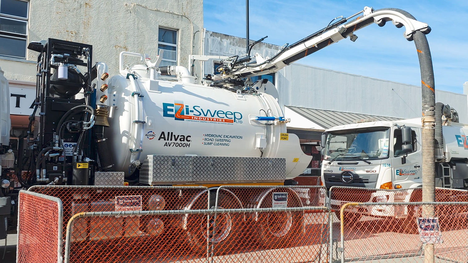 A man in hi-vis gear and a hard hat standing in front of an Allvac® AV7000H hydrovac truck and other drilling equipment on a construction site