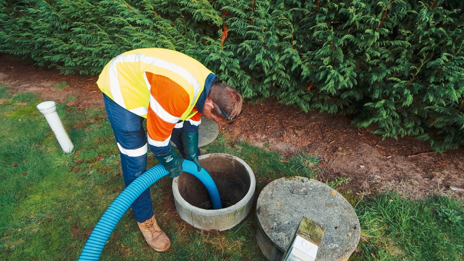 A man crouching next to a blue Moro Kaiser vacuum pump fitted on a vacuum tanker truck, talking to the camera.