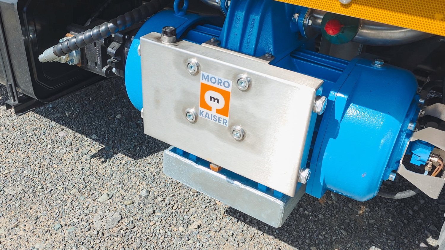 A man crouching next to a blue Moro Kaiser vacuum pump fitted on a vacuum tanker truck, talking to the camera.