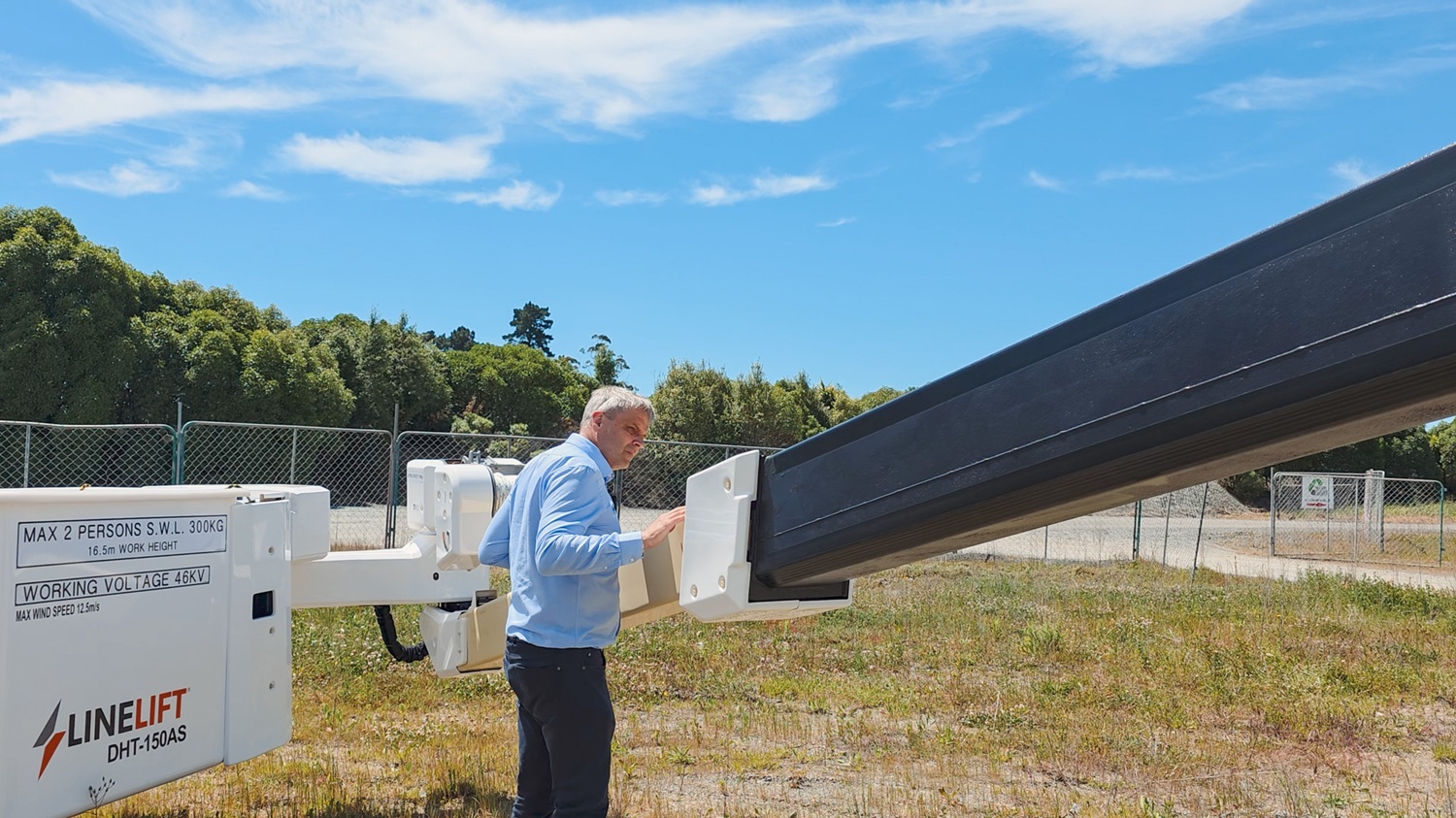 A man standing on a Linelift bucket truck in front of its insulated boom, explaining and pointing to the rear of the insulated boom