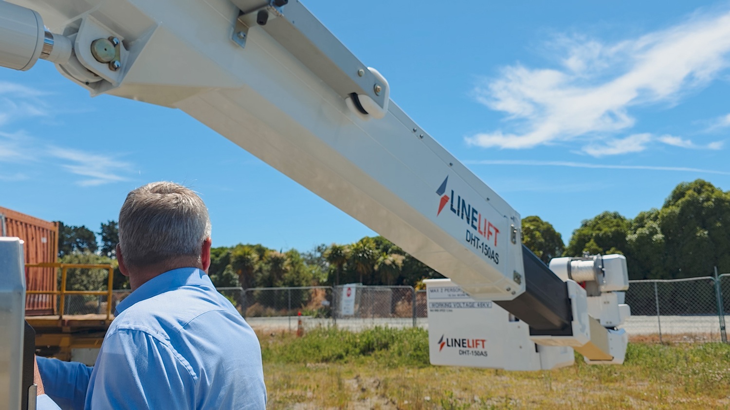 A man standing on a Linelift bucket truck in front of its insulated boom, explaining and pointing to the rear of the insulated boom