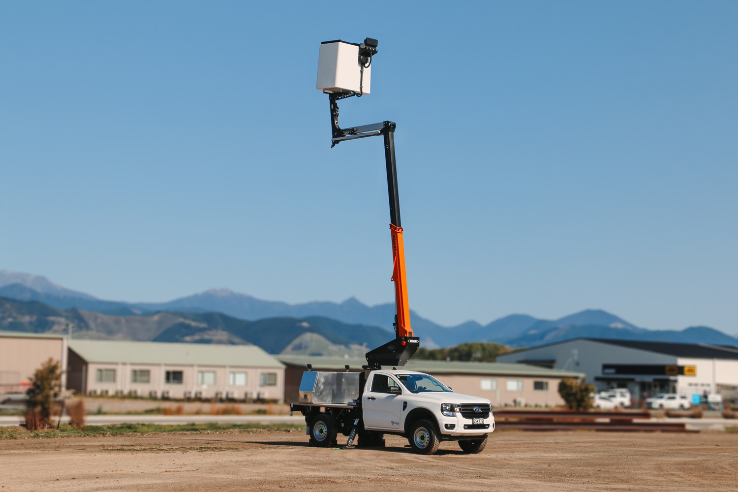 A compact white Ford Ranger ute with a Versalift crane and bucket mounted on the back for use in working at height, with toolboxes mounted on the deck.