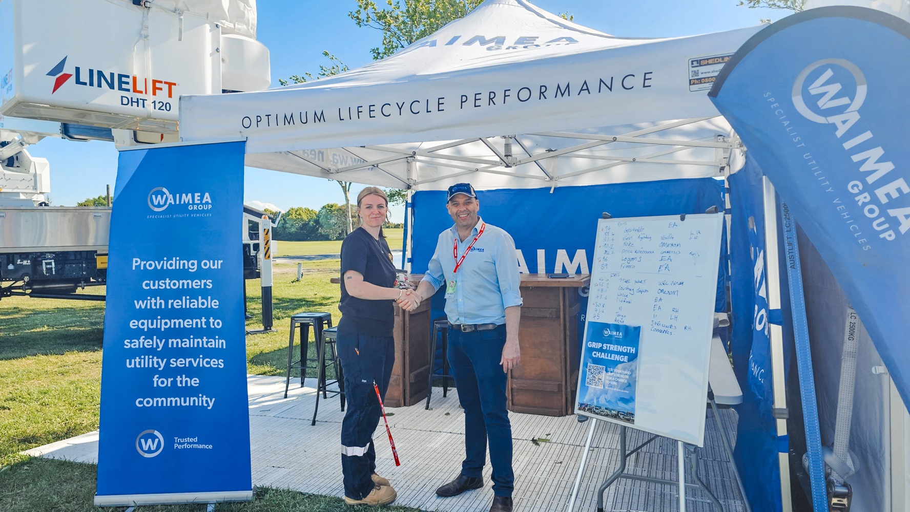 A showground viewed from up high, with lots of lines crane trucks set up with their crews demonstrating next to power poles, and stalls around the edge of the grounds, early in the morning.