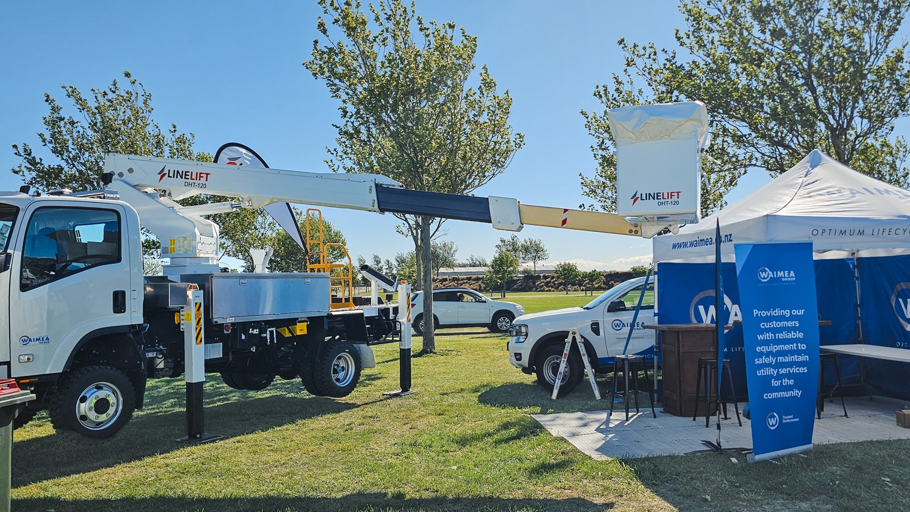 A showground viewed from up high, with lots of lines crane trucks set up with their crews demonstrating next to power poles, and stalls around the edge of the grounds, early in the morning.