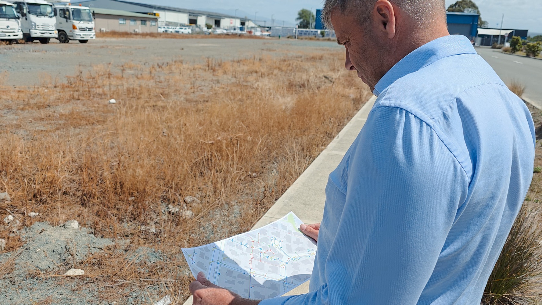 A specialist utility truck’s right rear outrigger is deployed on a grassy slope with a stabiliser pad and wedge to support it, with mudflaps on the wheels in the background with Waimea Group branding on them.