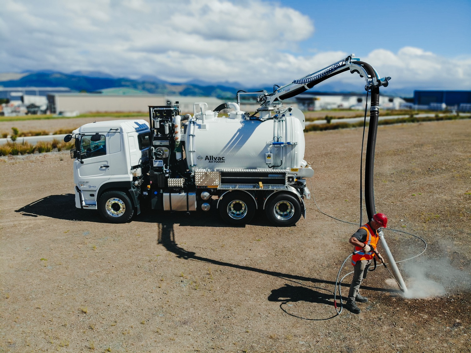 Two large white Allvac® hydrovac trucks with tanks and hose reels mounted on the back exiting the gate to a workyard. They are signwritten with Professional Excavation’s blue and green branding.