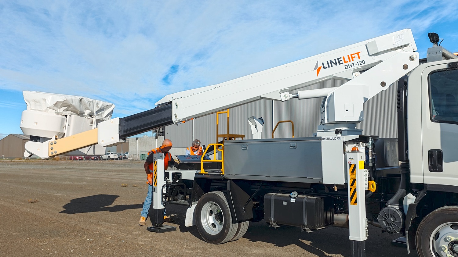 A man in a hi-vis vest stands in front of a white Linelift® bucket truck, which is parked in the background and has the boom and bucket extended into the foreground. The man is gesturing to the bucket.