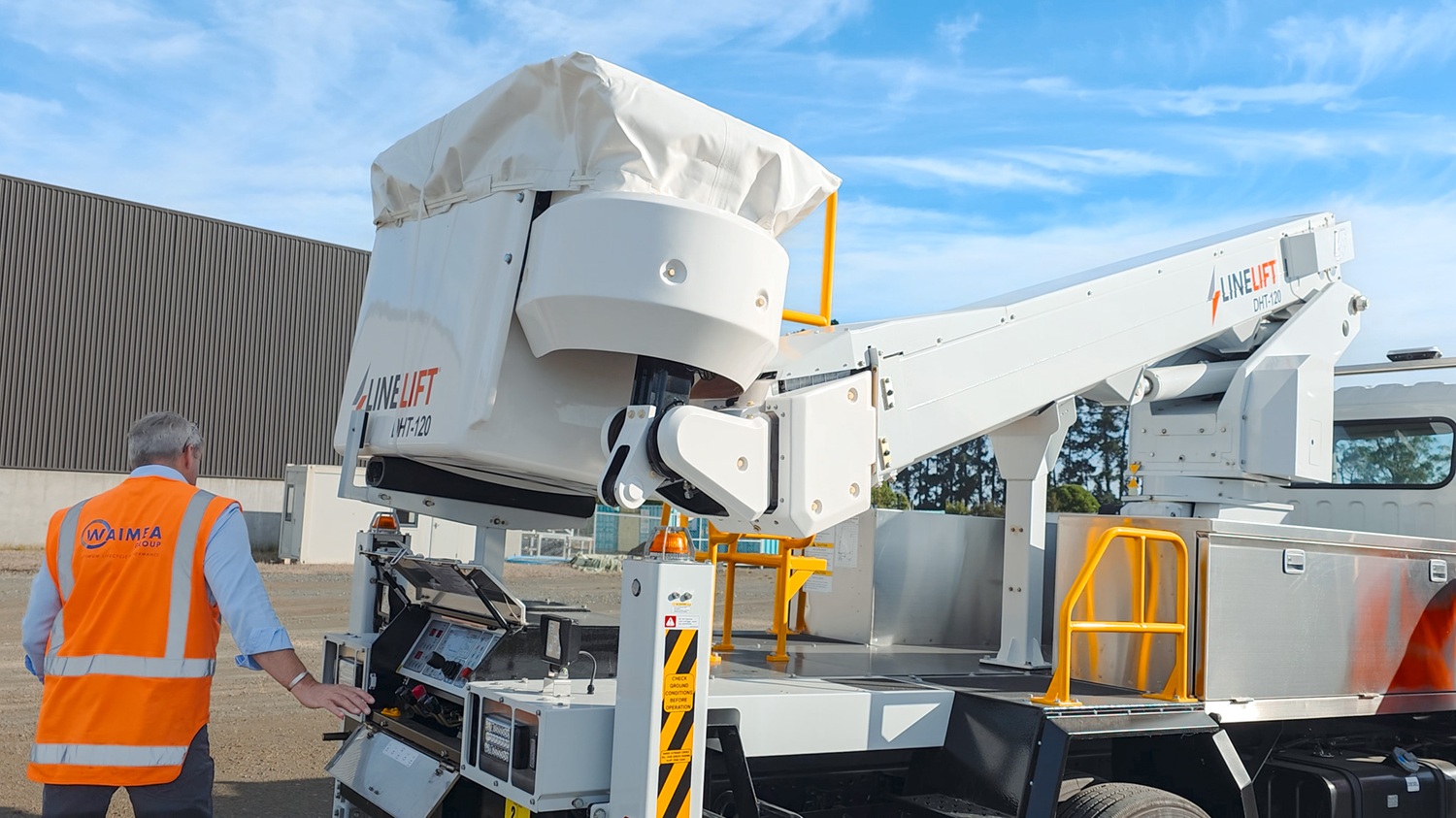 A man in a hi-vis vest stands in front of a white Linelift® bucket truck, which is parked in the background and has the boom and bucket extended into the foreground. The man is gesturing to the bucket.