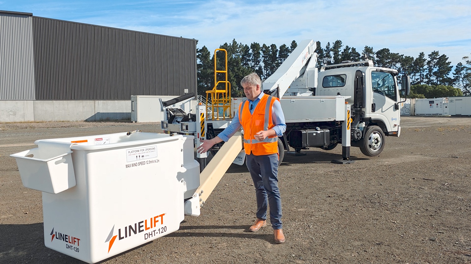 A man in a hi-vis vest stands in front of a white Linelift® bucket truck, which is parked in the background and has the boom and bucket extended into the foreground. The man is gesturing to the bucket.