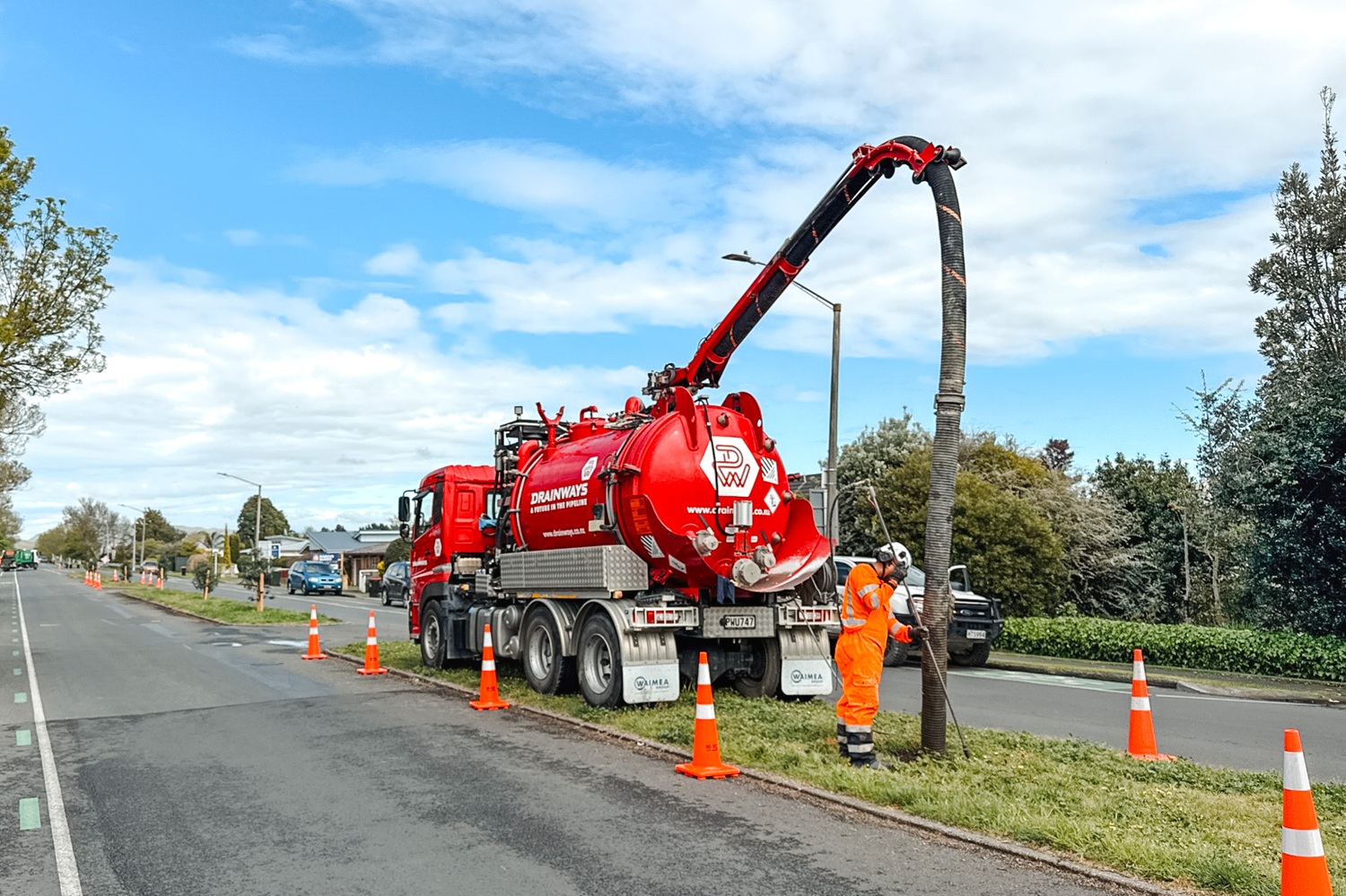 A large red hydrovac truck is parked on a riverbank with other excavation equipment, excavating holes for bridge foundations.