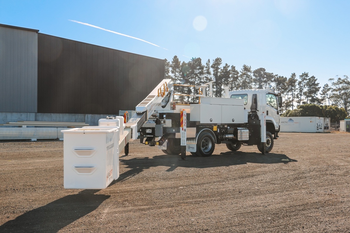 A white EWP truck parked in an empty lot, with a powerful Hino chassis, traction tyres, large sidemounted toolboxes, and an insulated bucket boom mounted on the back with Linelift DHT190AS branding, accessed by steps from the back with a railing.