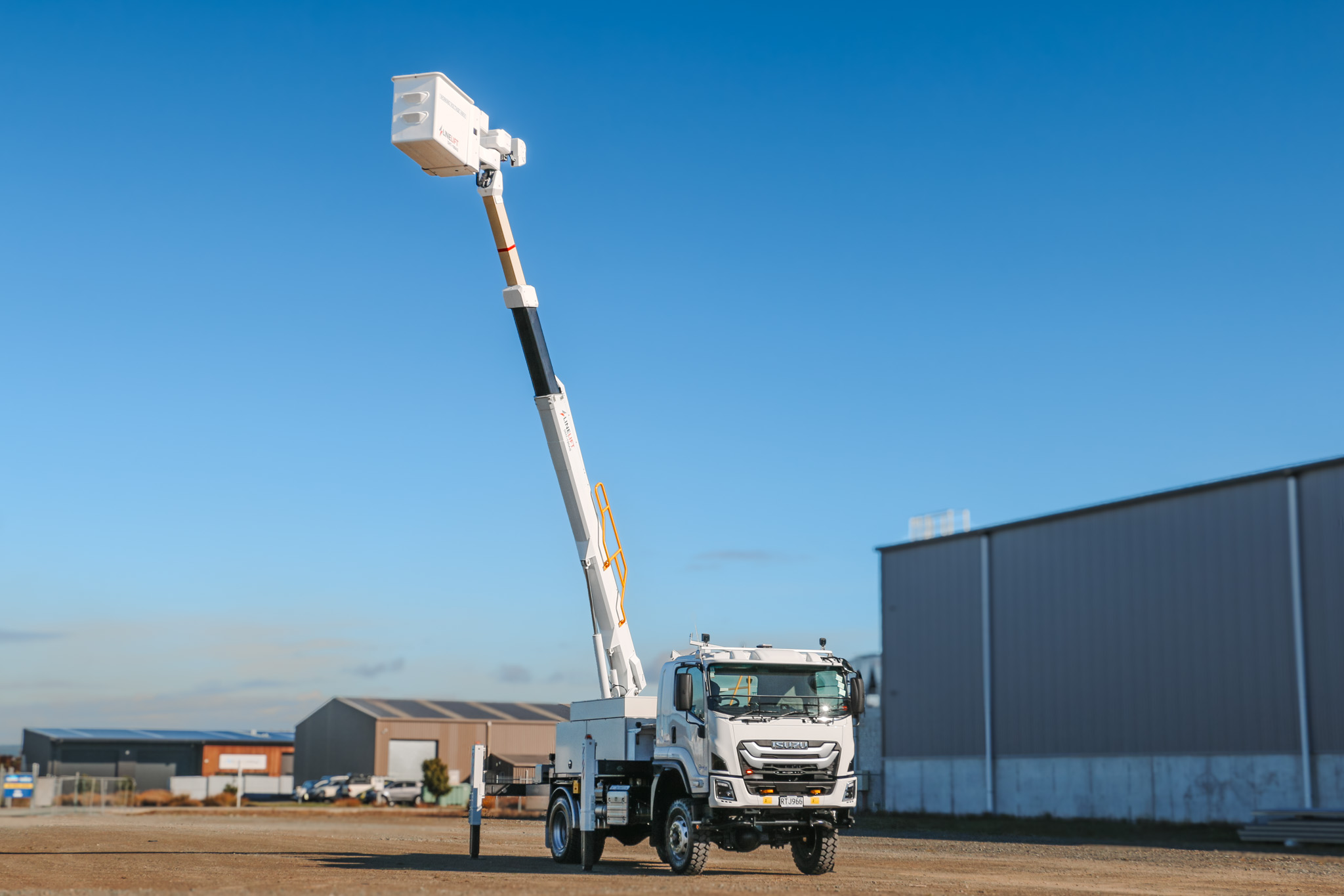 A white EWP truck parked in an empty lot, with a powerful Hino chassis, traction tyres, large sidemounted toolboxes, and an insulated bucket boom mounted on the back with Linelift DHT190AS branding, accessed by steps from the back with a railing.