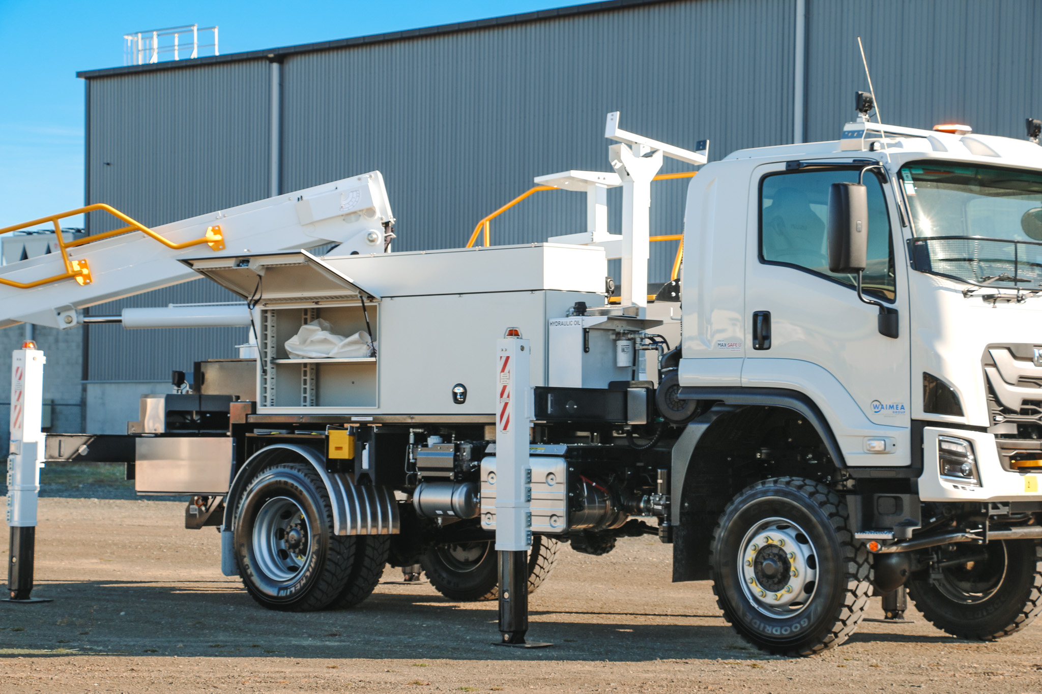 A white EWP truck parked in an empty lot, with a powerful Hino chassis, traction tyres, large sidemounted toolboxes, and an insulated bucket boom mounted on the back with Linelift DHT190AS branding, accessed by steps from the back with a railing.