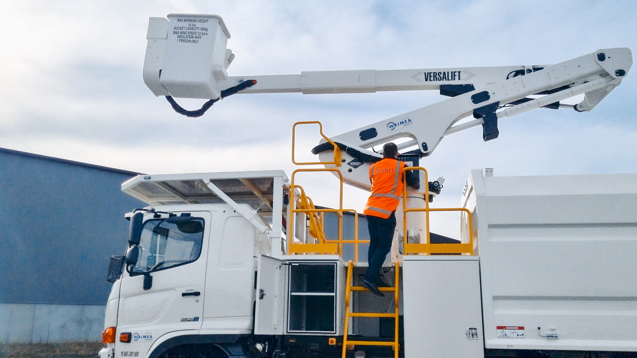 An EWP with a telescopic boom working on power lines in a field next to the treeline, with support utes around it.