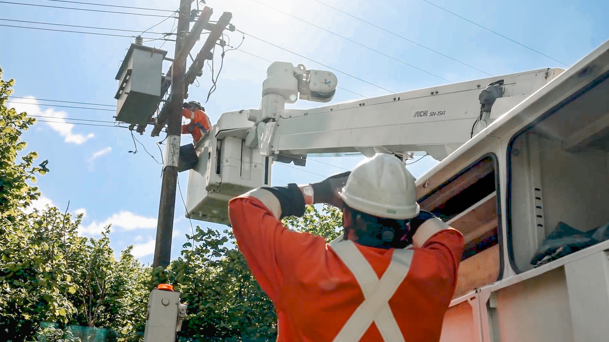An EWP with a telescopic boom working on power lines in a field next to the treeline, with support utes around it.
