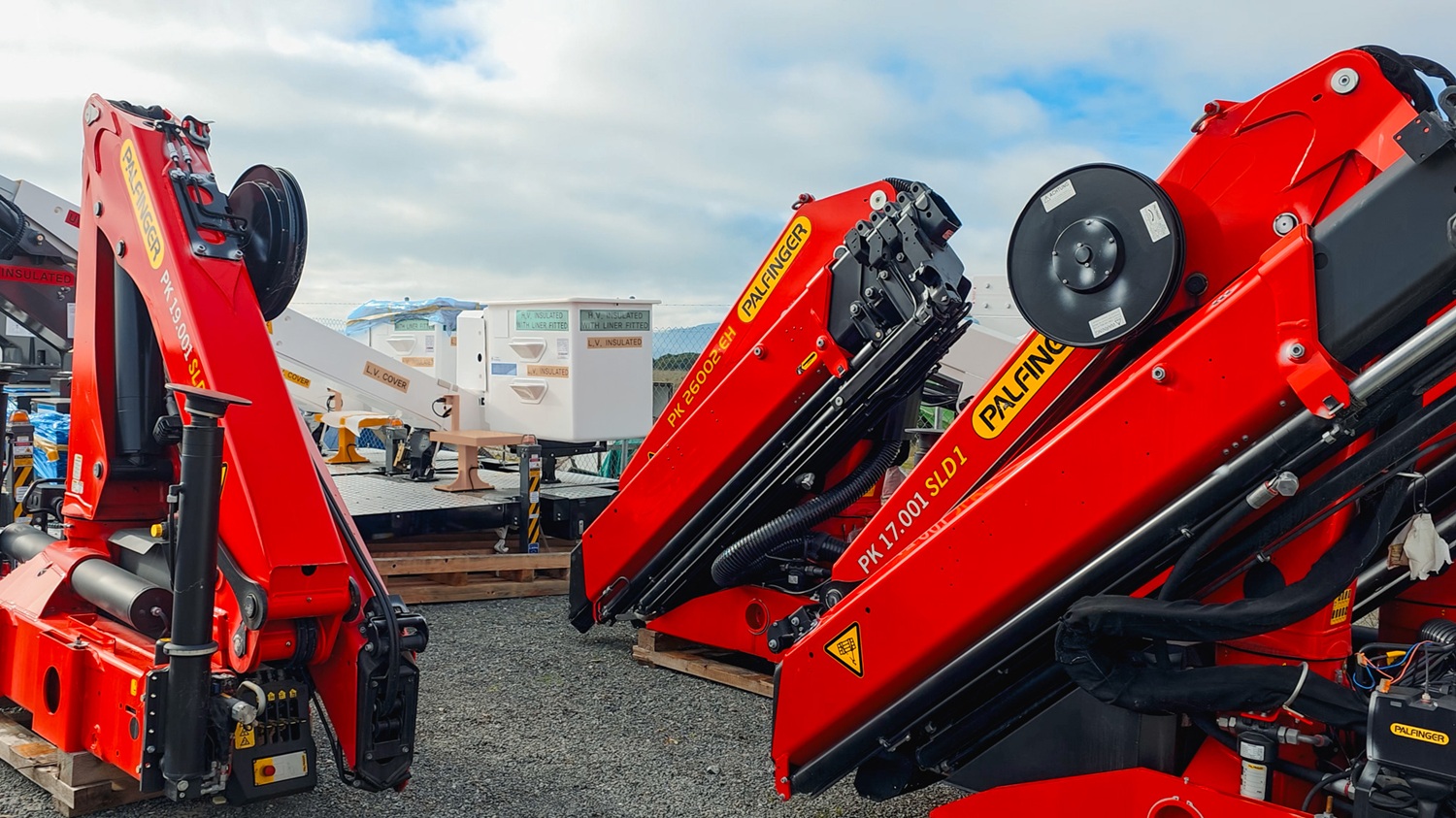 Three Palfinger knuckle boom craneds sitting in a yard, all different models.