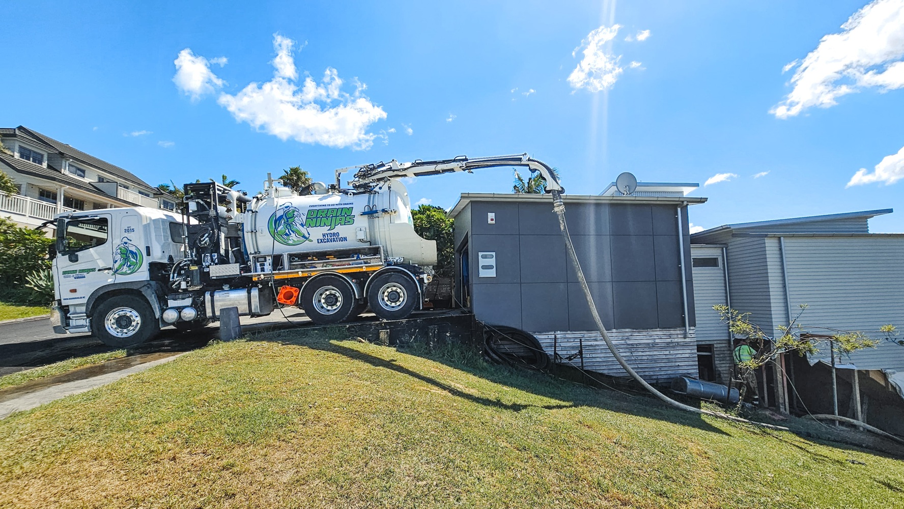 An Allvac® hydro excavator parked on a construction site with a blue hose extending from it several metres to the excavation site.