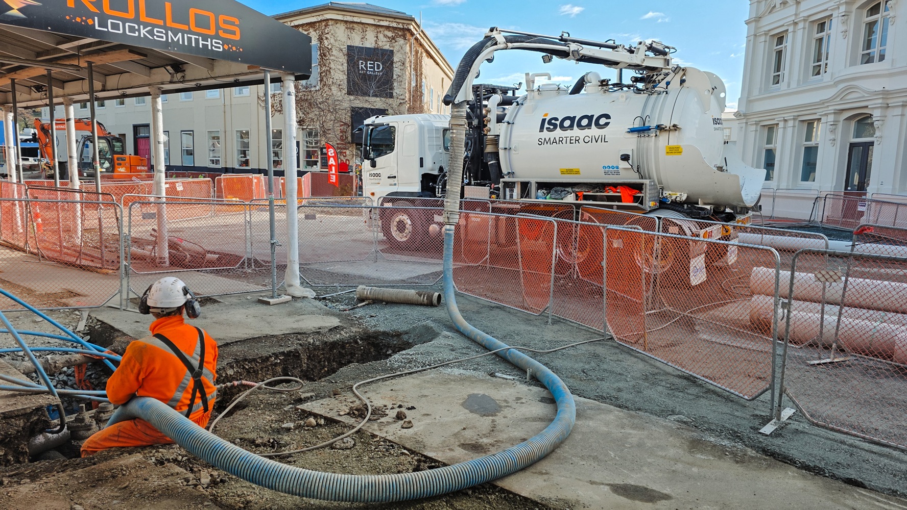 An Allvac® hydro excavator parked on a construction site with a blue hose extending from it several metres to the excavation site.