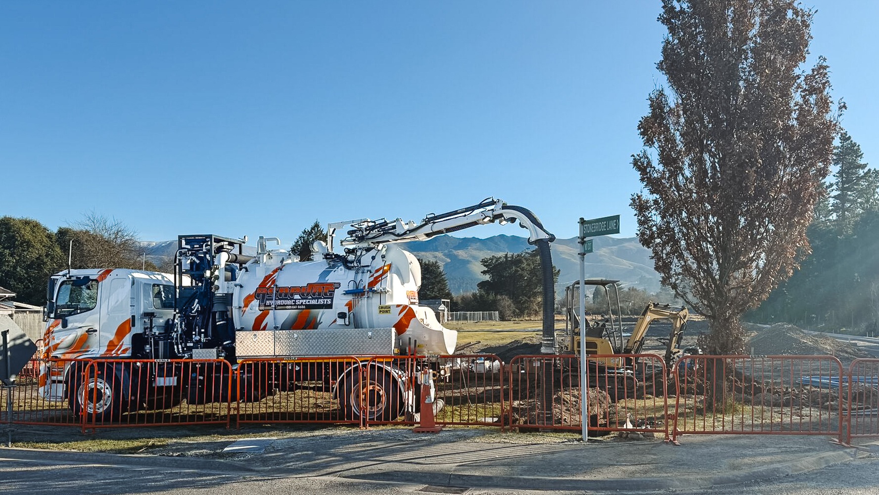 A white hydro excavation truck with custom signwriting in a parking lot with a dark cloudy sky behind it, showing the Allvac tank, overhead boom, and toolbox setup mounted on a Hino cab-chassis lit up by truck lights.